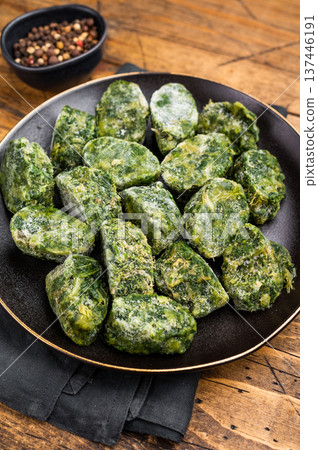 Raw, nutritious frozen spinach blocks on a dark plate, ready for thawing and cooking. Traditional rustic food photography. 137446191