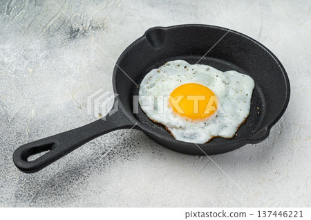Hot frying egg in cast iron pan, glowing yolk and white contrast on bright background. Classic brunch concept with simple rustic styling.. 137446221
