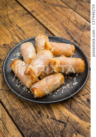 Fried spring rolls snack food on black plate with sesame topping overhead wooden background Fried spring rolls snack food on black plate with sesame topping overhead wooden background 137446259