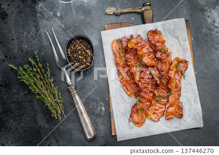 Smoked streaky bacon cooked to sizzling crispness with shiny pork surface resting on parchment and herbs great for culinary designs. 137446270