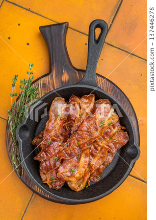 Glossy roasted Streaky bacon strips served in black skillet with fresh thyme over rustic yellow surface ideal for menus and food ads. Glossy roasted Streaky bacon strips served in black skillet with fresh thyme over rustic yellow surface ideal for menus and food ads. 137446278