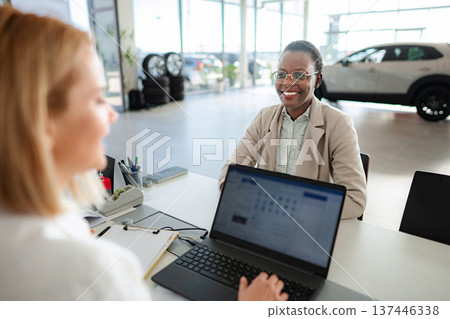 Car salesperson consulting client at modern dealership desk 137446338