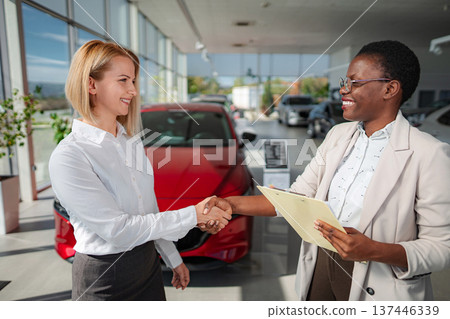 Saleswoman and customer shaking hands making car deal Saleswoman and customer shaking hands making car deal 137446339