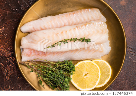 Raw cod loin pieces, whitefish fillets without skin on plate with herbs. brown background. top view Raw cod loin pieces, whitefish fillets without skin on plate with herbs. brown background. top view 137446374