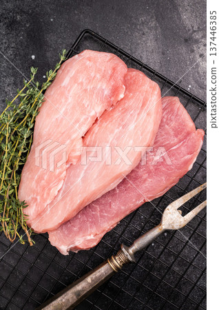 Raw pork fillet meat for schnitzel, steaks on a rack. black background. top view Raw pork fillet meat for schnitzel, steaks on a rack. black background. top view 137446385