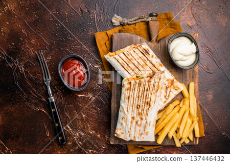 Shawarma chicken roll with fresh vegetables, cream sauce and french fries on wooden board. brown background. top view 137446432