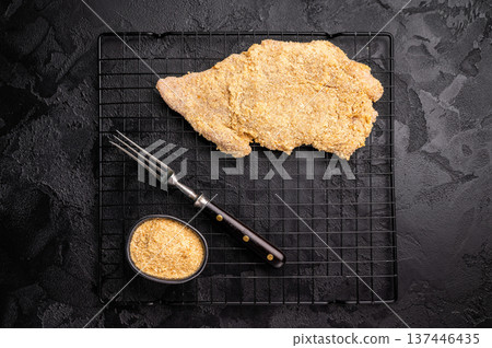 Raw breaded pork Schnitzel steak on a rack. black background. top view Raw breaded pork Schnitzel steak on a rack. black background. top view 137446435