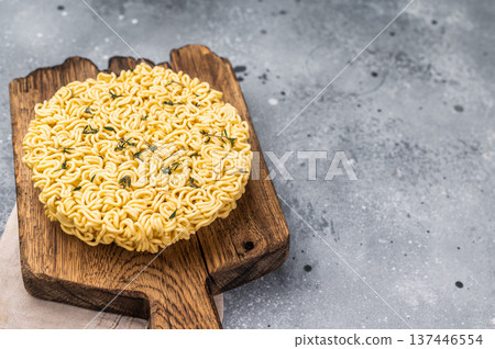 Twisted raw ramen noodles, ready to soak up flavors and bring warmth to your next culinary adventure. grey background. top view Twisted raw ramen noodles, ready to soak up flavors and bring warmth to your next culinary adventure. grey background. top view 137446554