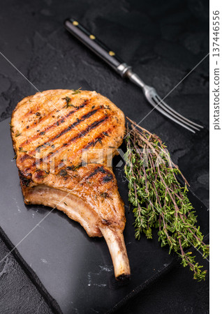 Savory bone in pork chop steak, beautifully charred and ready to impress at your next barbecue gathering. black background. top view Savory bone in pork chop steak, beautifully charred and ready to impress at your next barbecue gathering. black background. top view 137446556