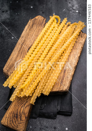 Uncooked mafaldine, ready to be transformed into a delicious dish that highlights its delightful texture. black background. top view Uncooked mafaldine, ready to be transformed into a delicious dish that highlights its delightful texture. black background. top view 137446583