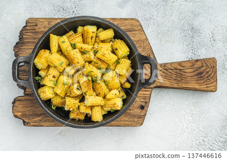 Roasted baby corn sliced into pieces with seasoning and thyme in skillet overhead on textured background 137446616