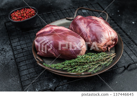 Fresh veal hearts displaying dense myocardium and natural marbling arranged with herbs and spices on rustic dark surface. 137446645
