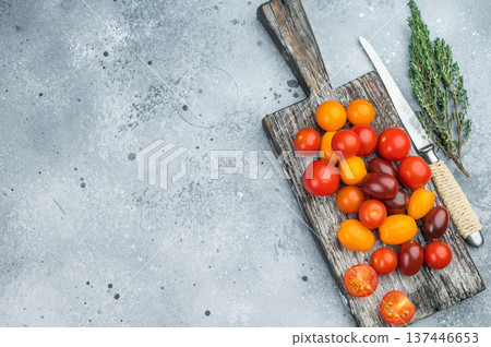 Colorful mix of cherry tomatoes on a rustic wooden board with herbs and knife on a textured gray background perfect for food templates. Colorful mix of cherry tomatoes on a rustic wooden board with herbs and knife on a textured gray background perfect for food templates. 137446653