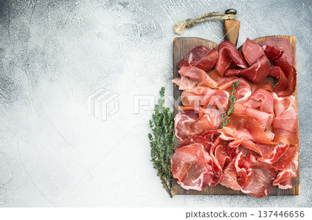 Italian charcuterie with prosciutto, coppa and bresaola arranged on a rustic wooden board with thyme, shot top view on a light textured background. 137446656