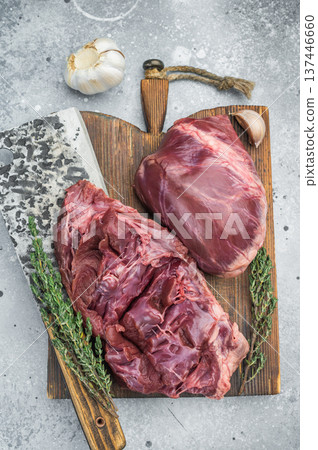 Whole and cut pork hearts highlighting anatomy muscle fibers and valves with garlic thyme and chopping cleaver nearby. 137446660