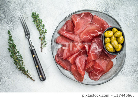 Gourmet Italian bresaola charcuterie with green olives and herbs, presented on a stone textured background for elegant flat lay. Gourmet Italian bresaola charcuterie with green olives and herbs, presented on a stone textured background for elegant flat lay. 137446663