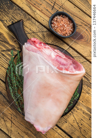 Raw pork knuckle hock with rind bone and muscle fibers on rustic board with thyme salt and meat fork ideal for butchery prep and culinary detailing. Raw pork knuckle hock with rind bone and muscle fibers on rustic board with thyme salt and meat fork ideal for butchery prep and culinary detailing. 137446664