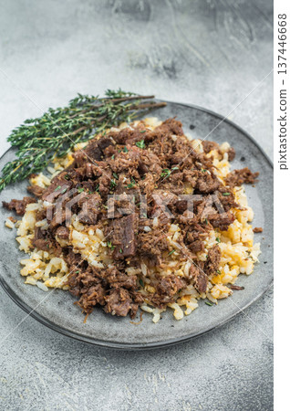 Kawurma served on pilaf featuring roasted meat chunks, gelatin breakdown, savory seasoning and macro visible texture in overhead view. 137446668