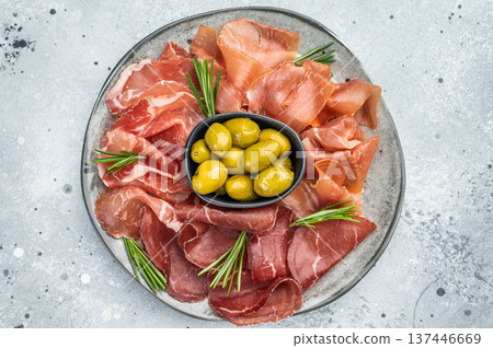 Bresaola, prosciutto and coppa slices with green olives on a rustic gray background, perfect for Mediterranean food visuals. Bresaola, prosciutto and coppa slices with green olives on a rustic gray background, perfect for Mediterranean food visuals. 137446669