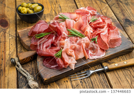 Premium dry cured meats on rustic wood: prosciutto, coppa and bresaola garnished with rosemary and green olives, overhead shot. Premium dry cured meats on rustic wood: prosciutto, coppa and bresaola garnished with rosemary and green olives, overhead shot. 137446683
