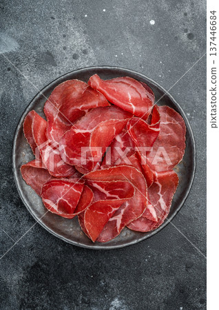 Lean marbled dried beef cecina arranged on a dark plate against a gray concrete surface, showcasing premium charcuterie texture. Lean marbled dried beef cecina arranged on a dark plate against a gray concrete surface, showcasing premium charcuterie texture. 137446684