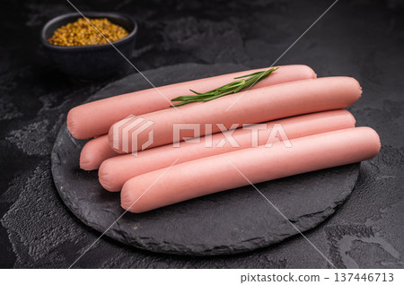 Raw hot dog sausages (frankfurters/wieners) on a dark stone background with grain mustard. Ideal for restaurant menus and food ads. 137446713