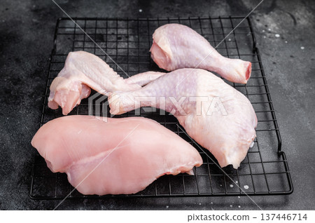Assortment of fresh raw chicken meat on a metal rack over a textured black surface. High angle view with generous copy space. 137446714