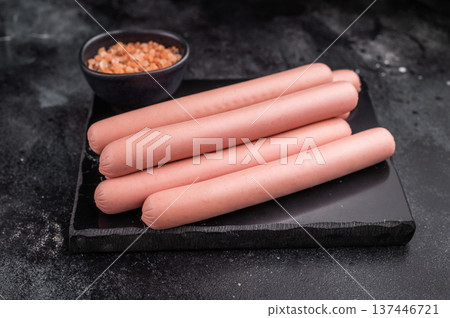 Four raw pink hot dog sausages (frankfurters/wieners) on a contrasting dark stone background with Himalayan salt. Copy space. Four raw pink hot dog sausages (frankfurters/wieners) on a contrasting dark stone background with Himalayan salt. Copy space. 137446721