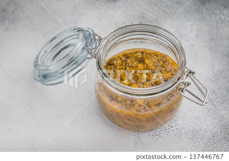 Cucumber relish preserve in glass jar with spoon and thyme on wooden board light stone background overhead view. 137446767