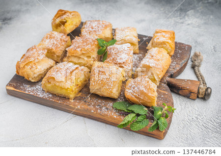 Greek custard pie bougatsa made with flaky filo pastry sliced into squares served on wooden board with powdered sugar Greek custard pie bougatsa made with flaky filo pastry sliced into squares served on wooden board with powdered sugar 137446784