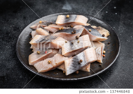 Pickled herring chunks cured in salt and brine served with spices and herbs. Traditional seafood on dark textured background. 137446848