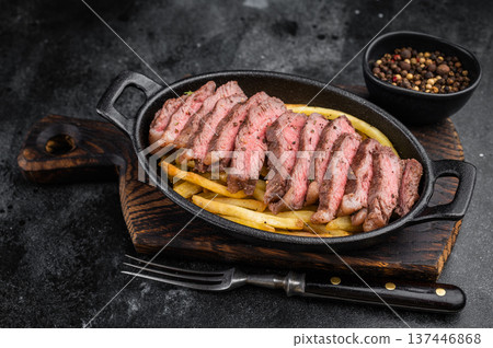 Medium rare beef picanha steak cut into slices with crispy fries in rustic skillet, overhead restaurant style meal 137446868