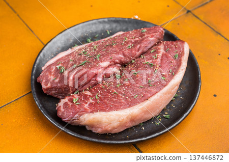 Raw beef culotte steaks also called picanha or rump cap on black ceramic plate, bright yellow stone background 137446872