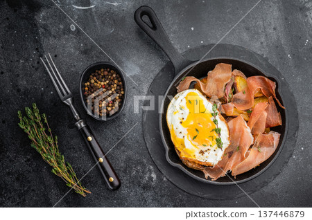 Huevos rotos con jamon with fried potatoes and runny egg cooked in cast iron skillet top view on dark stone background Huevos rotos con jamon with fried potatoes and runny egg cooked in cast iron skillet top view on dark stone background 137446879