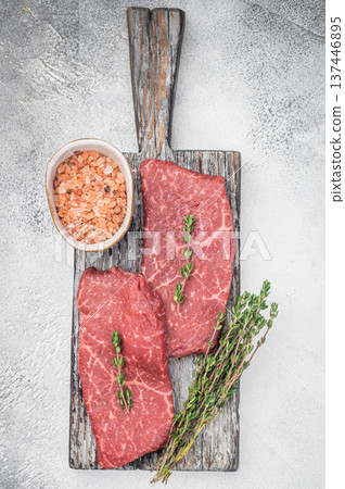 Uncooked chuck flatiron beef steaks with thyme sprigs and seasoning on vintage board overhead minimal composition Uncooked chuck flatiron beef steaks with thyme sprigs and seasoning on vintage board overhead minimal composition 137446895
