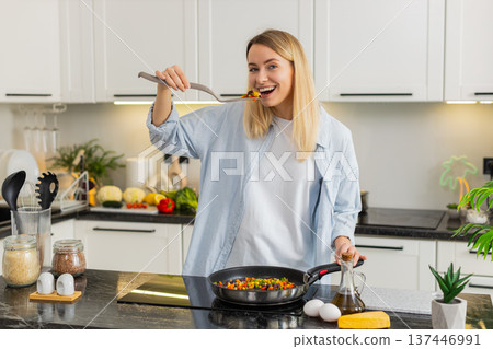 Young woman tasting sauteed vegetables in skillet on electric stove for keto diet home kitchen meal Young woman tasting sauteed vegetables in skillet on electric stove for keto diet home kitchen meal 137446991