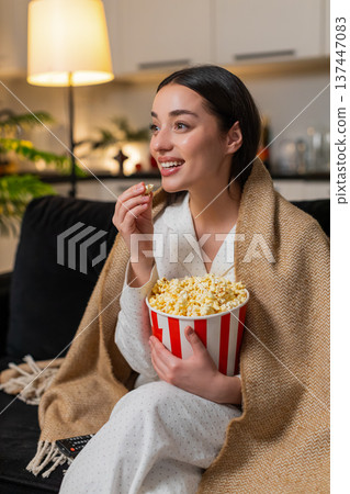 Young woman in blanket with popcorn laughs at movie or online show comments reacts cheerful evening 137447083
