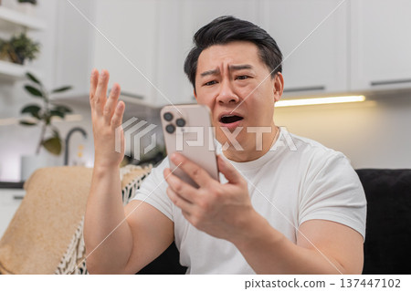 Asian man loses game on smartphone sighs in defeat frowns at bad news and shares reply in chat sad Asian man loses game on smartphone sighs in defeat frowns at bad news and shares reply in chat sad 137447102
