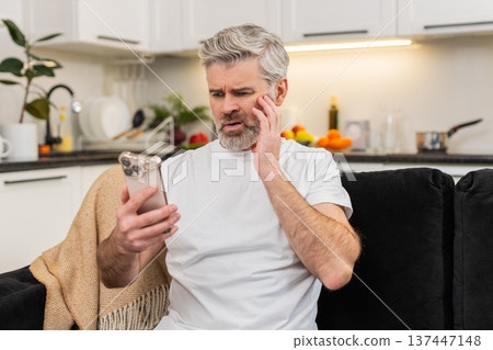 Middle-aged man frowns at smartphone sees failed game and job refusal shakes head no in frustration 137447148