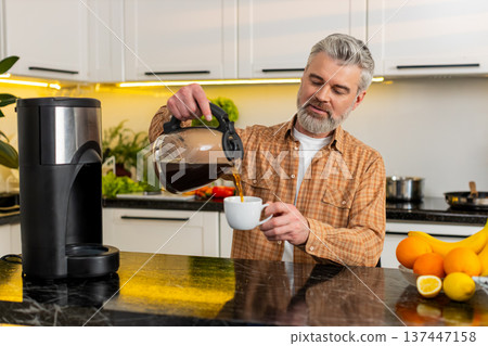 Middle-aged man pours fresh coffee from machine in kitchen enjoying morning routine energy at home Middle-aged man pours fresh coffee from machine in kitchen enjoying morning routine energy at home 137447158