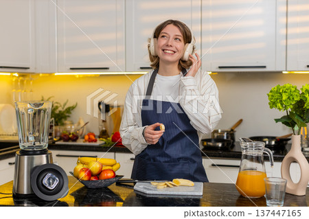 Young woman listening to music while making smoothie in kitchen during healthy meal prep work break Young woman listening to music while making smoothie in kitchen during healthy meal prep work break 137447165