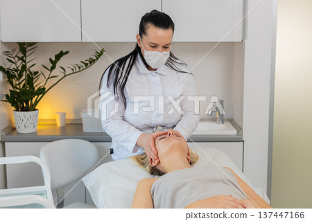 Woman having relaxing forehead massage procedure by professional beautician in cosmetology clinic Woman having relaxing forehead massage procedure by professional beautician in cosmetology clinic 137447166
