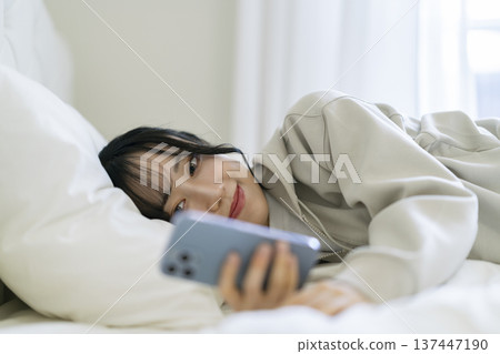A young woman lying down and staring at her smartphone screen A young woman lying down and staring at her smartphone screen 137447190