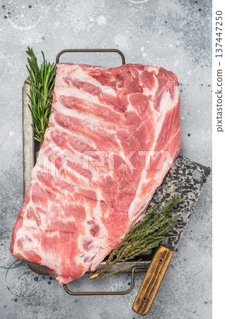Raw pork spareribs slab on metal tray with herbs and knife flat lay on gray stone background rustic cooking concept. Raw pork spareribs slab on metal tray with herbs and knife flat lay on gray stone background rustic cooking concept. 137447250