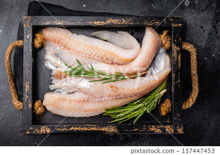Ready for cooking Raw Hake fish fillets in a wooden tray with herbs. black background. top view 137447453