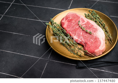 Raw Striploin steak, New York strip beef steak in a plate with herbs. black background. top view 137447480