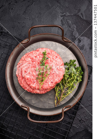 Stack of Raw meat patties, cutlets, chopped meat for burgers in stell tray with herbs. black background. top view 137447501