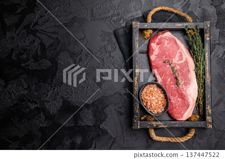 Raw New York strip beef steak in a wooden tray with herbs. black background. top view Raw New York strip beef steak in a wooden tray with herbs. black background. top view 137447522