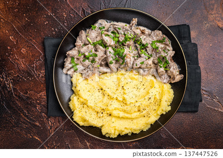 Beef stroganoff with mashed potatoes, fresh greenery and savory mushroom sauce in a plate . brown background. top view Beef stroganoff with mashed potatoes, fresh greenery and savory mushroom sauce in a plate . brown background. top view 137447526
