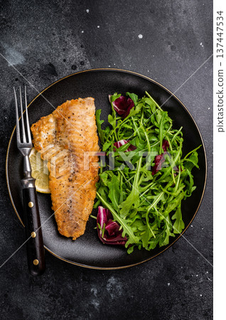 Roasted Haddock fish fillet on a plate with salad. black background. top view 137447534